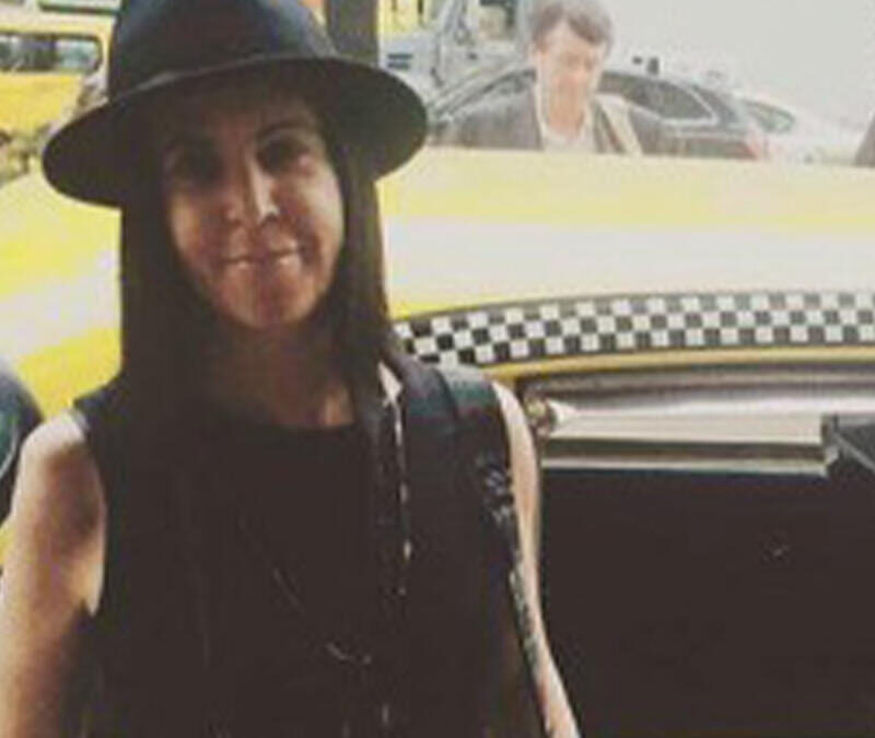A woman in a black hat standing next to a yellow taxi.