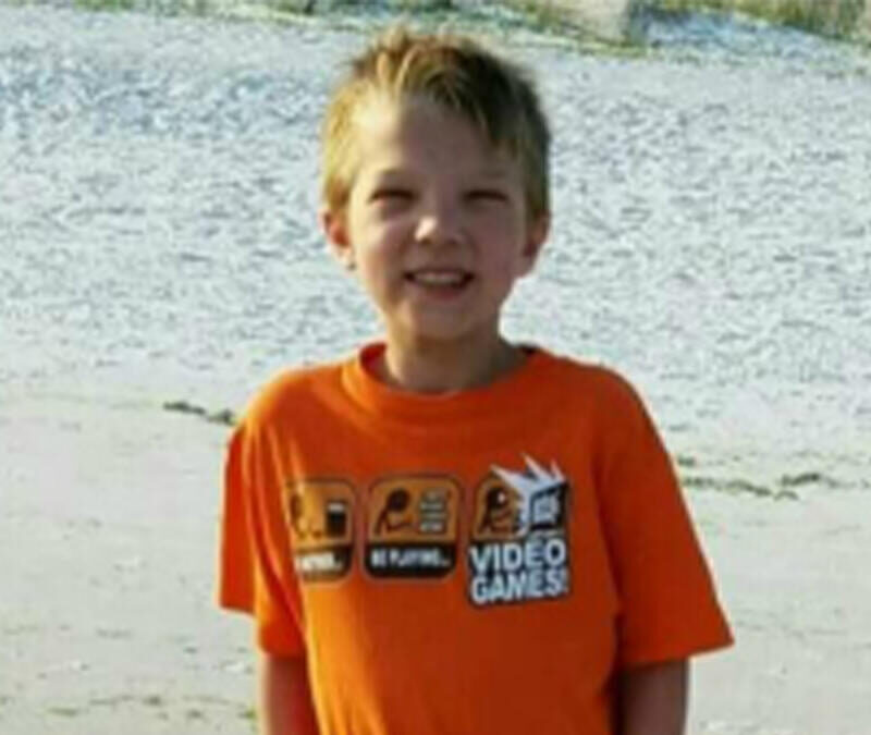 A young boy in an orange shirt standing on the beach.