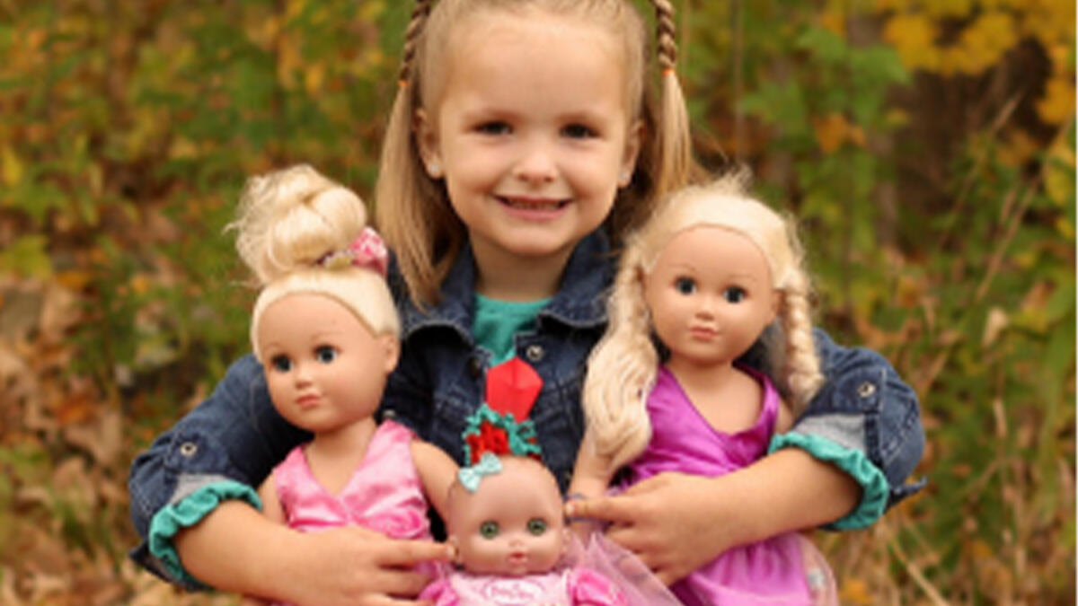 A little girl holding three dolls in the fall.