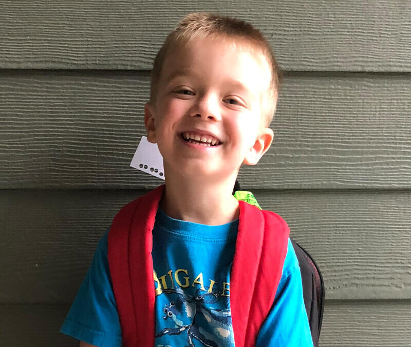 A young boy wearing a backpack and smiling.