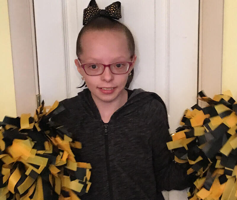 A girl with glasses and pom poms standing in front of a door.