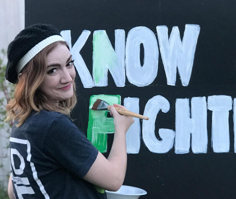 A girl painting a sign that says know fighter.