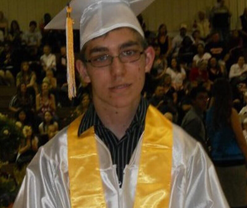 A young man in a graduation gown standing in front of a crowd.