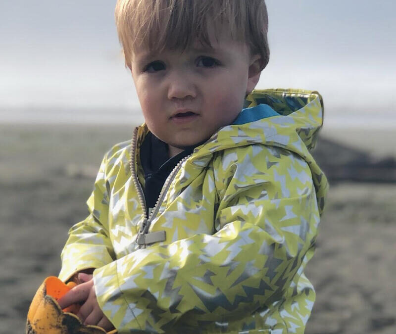 A young boy in a yellow jacket standing on a beach.