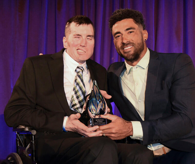 A man in a wheelchair is holding an award with a man in a suit.