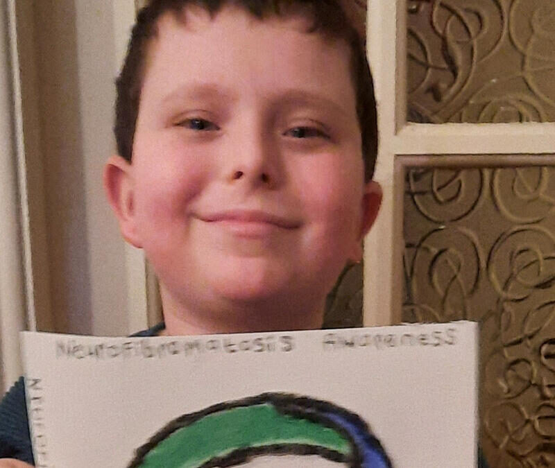 A young boy holding up a drawing of the letter c.