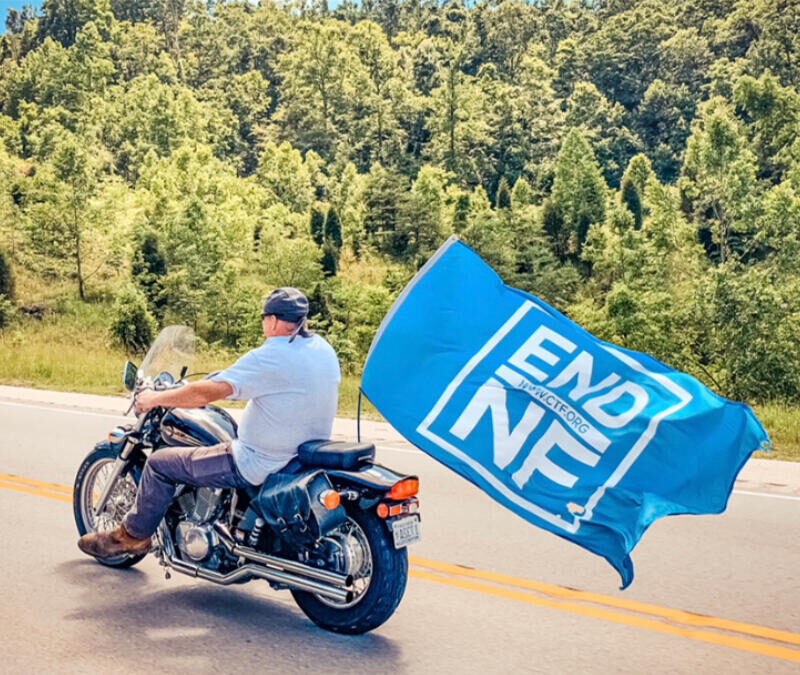 A man on a motorcycle with a flag.