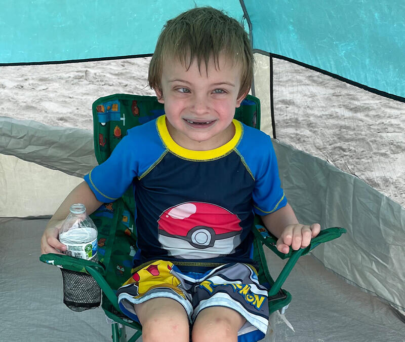 A young boy sitting in a chair in front of a tent.