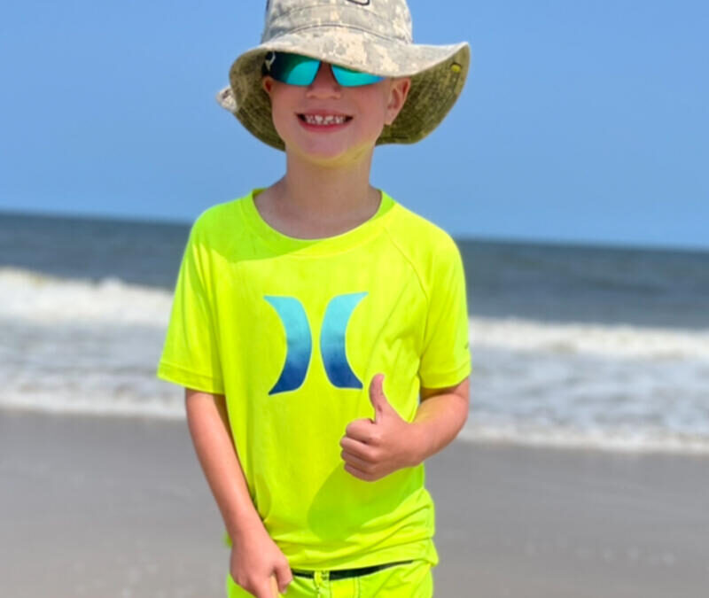 A young boy wearing a yellow hat and sunglasses on the beach.