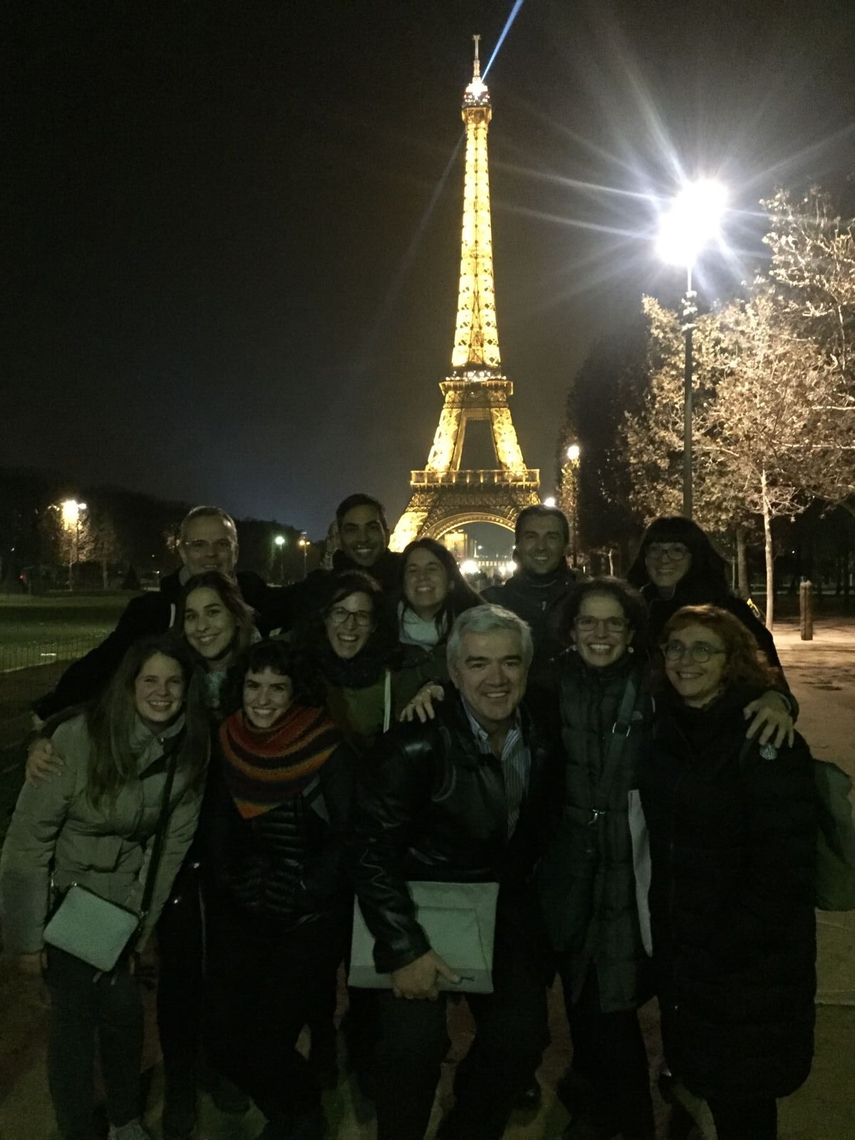 A group of people posing for a photo at night in front of the illuminated Eiffel Tower.