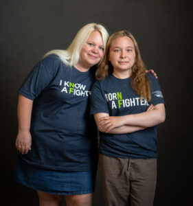 Two people standing together, smiling at the camera, wearing t-shirts with empowering slogans, against a dark background.