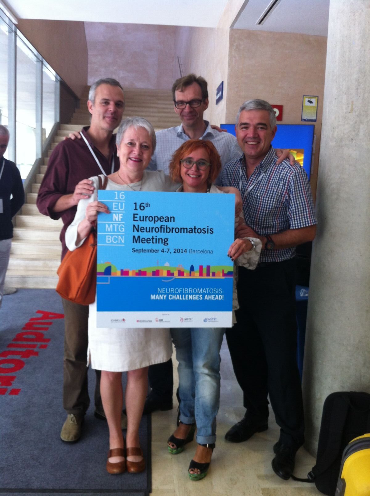 Five people standing indoors holding a sign for the 16th European Neurofibromatosis Meeting held in Barcelona from September 4-7, 2014.