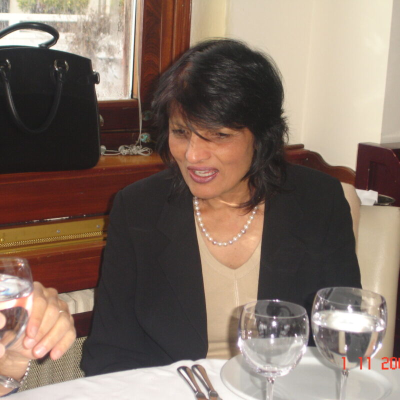 A woman in a beige top and black blazer is sitting at a table with a white tablecloth, engaged in conversation. There are glasses of water and a black handbag on the table. Photo date is November 1, 2009.