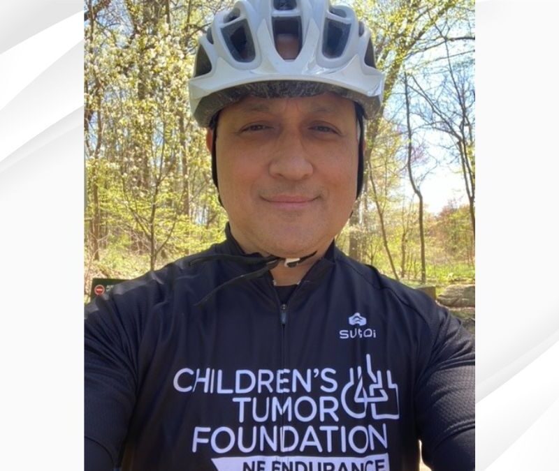 Person wearing a helmet and a cycling jersey that reads "Children's Tumor Foundation, NF Endurance," standing outdoors with trees in the background.