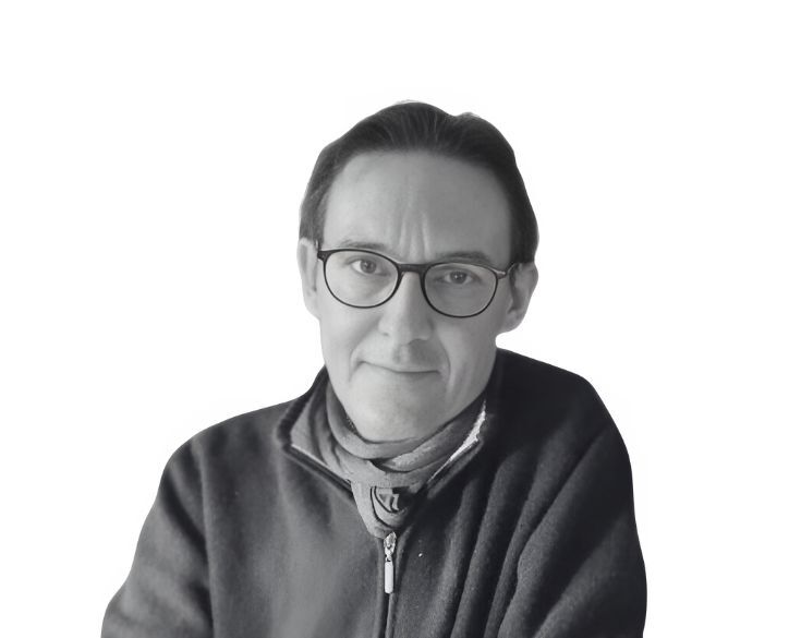 A black-and-white photo of a person with glasses, wearing a zipped-up sweater and a neck scarf, against a plain white background.