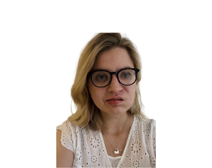 A person with blonde hair and glasses is wearing a white eyelet top and a necklace, looking into the camera against a plain white background.