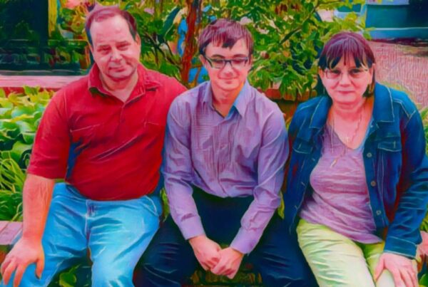 Three people sitting on a brick ledge in a garden, with plants in the background.