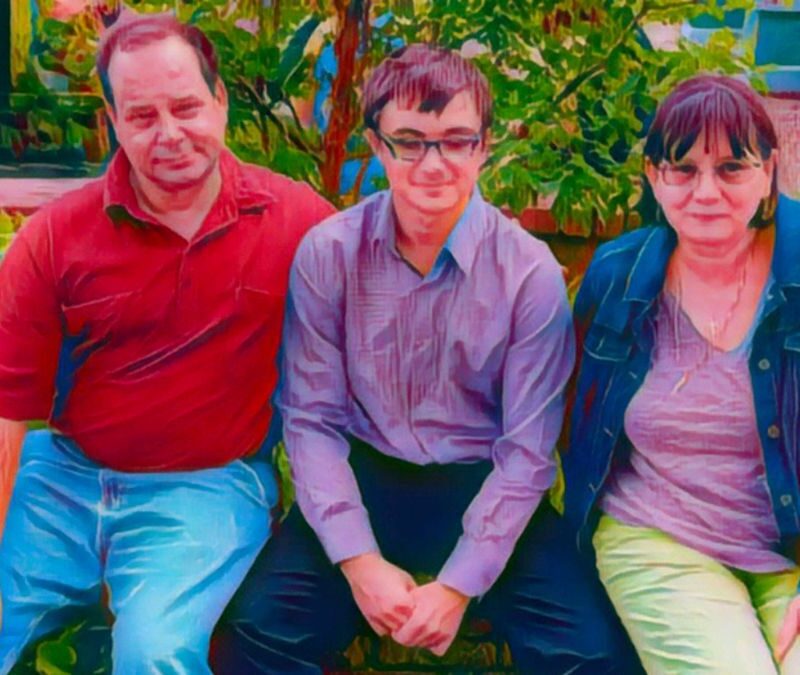 Three people sitting on a brick ledge in a garden, with plants in the background.