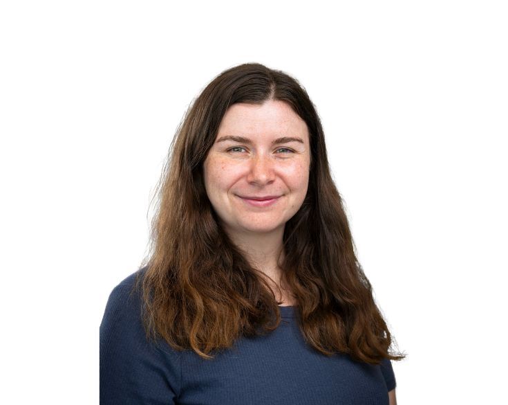 A woman with long brown hair in a blue shirt smiles at the camera against a white background.