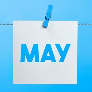 A white card with "MAY" in blue letters is clipped to a blue clothesline against a blue background.