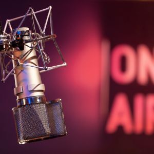 A microphone in a recording studio with a blurred "On Air" sign in the background.