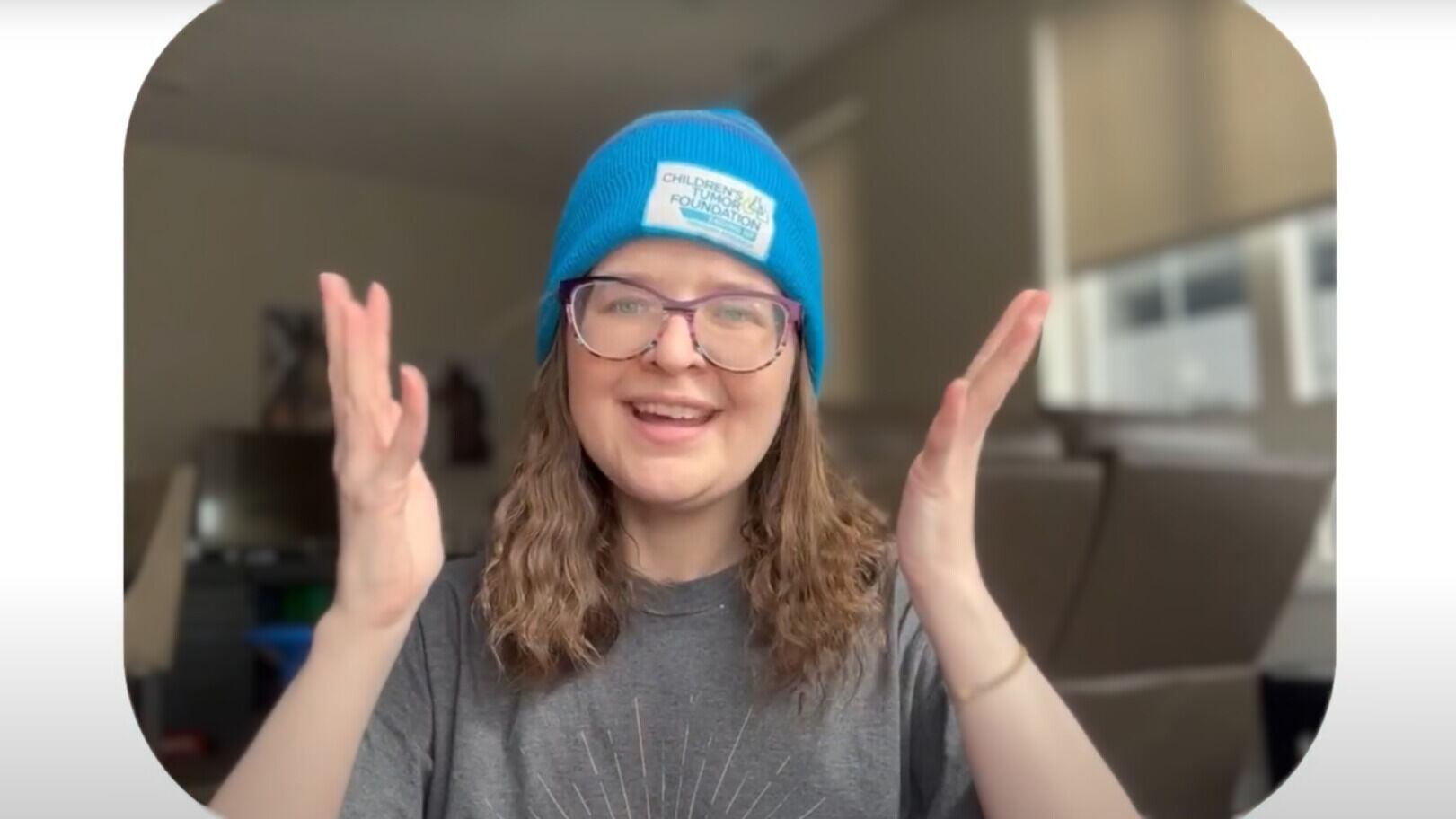 Person wearing glasses and a blue beanie, gesturing with both hands, indoors.