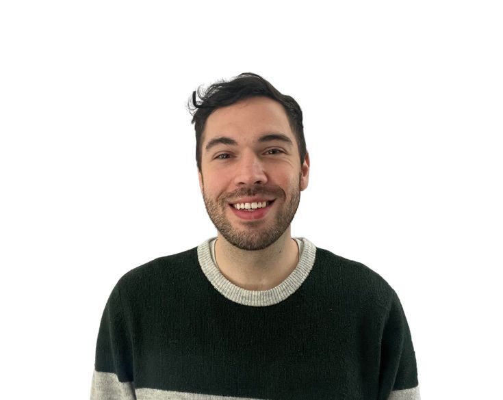 A person with dark hair and a beard smiling, wearing a dark green and gray striped sweater, against a plain white background.